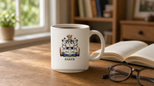 
Load image into Gallery viewer, White 11oz Heritage Mug with the Baker coat of arms and surname on a wooden desk by a window (illustrative photo)